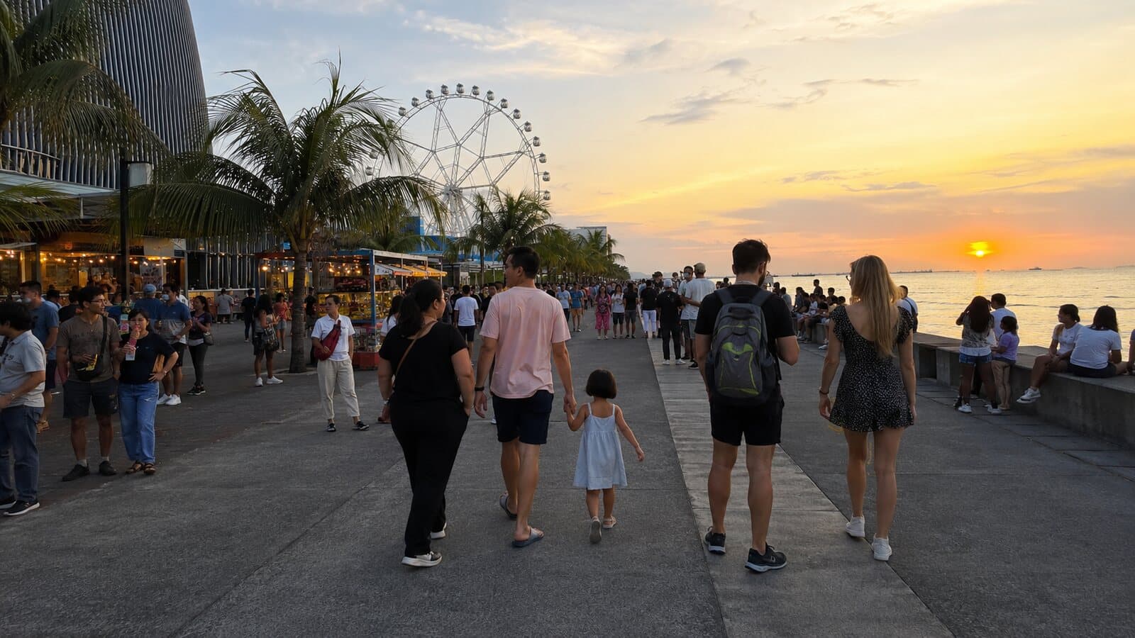 Families walking on the Manila Bay promenade near the MOA district at sunset