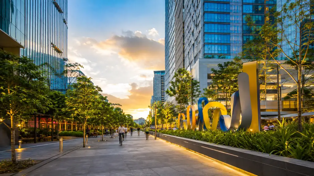 Bonifacio Global City pedestrian boulevard with modern towers, tropical trees and public art at sunset