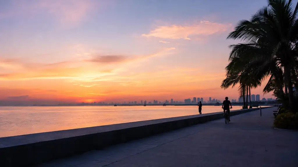 Pastel sunrise over Manila Bay with palms, distant skyline, cyclist and photographer silhouettes